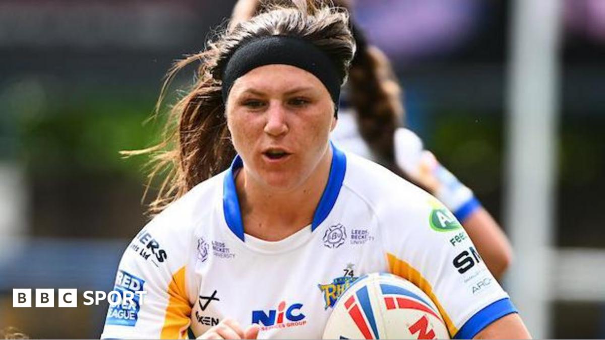 Leeds Rhinos player Connie Boyd, in white, blue and gold and wearing a hairband, carries the ball.