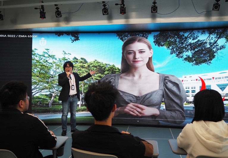 Pan Hui stands next to a digital teaching avatar on a big screen.