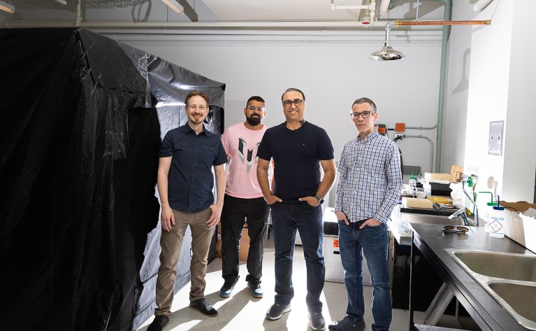 Four men standing next to a dark tent in a lab.