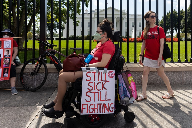 A woman in a wheelchair wearing a facemask and other protestors seen outside of the White House, with placards to draw attention to those that are suffering from long covid.