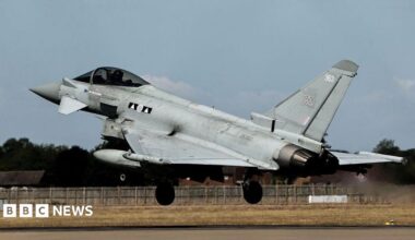 A grey Typhoon jet takes off on a runway with streams coming out of its exhaust.