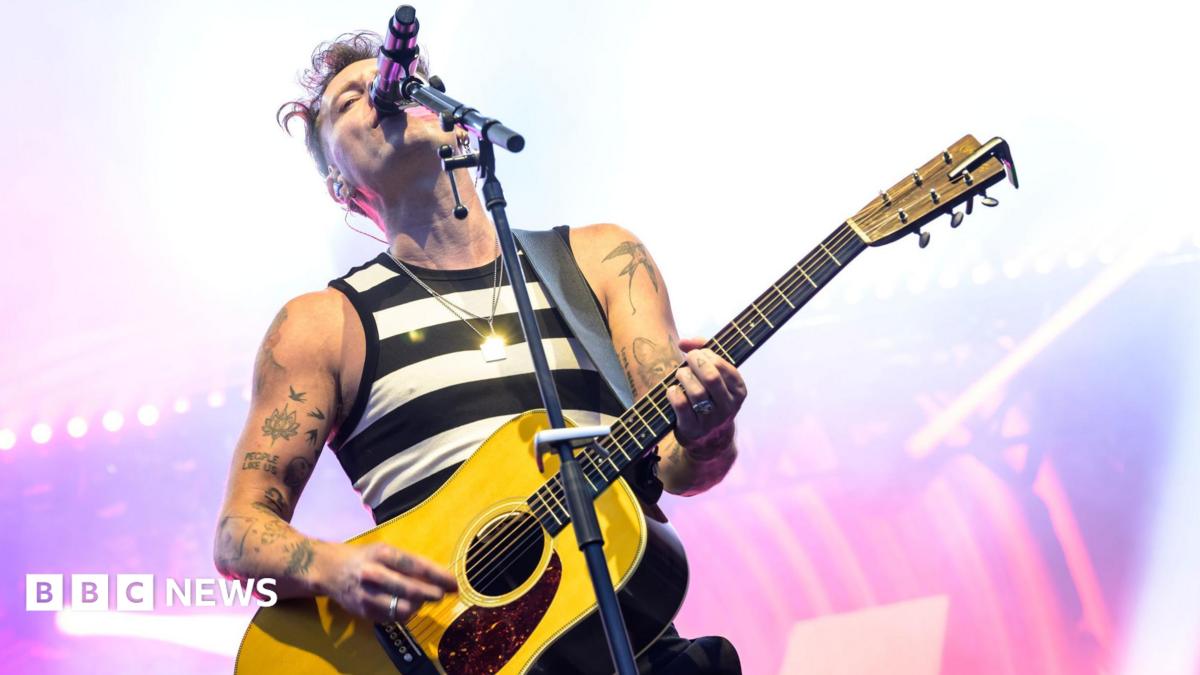 Scottish singer-songwriter Callum Beattie is performing on a stage. He is wearing a black and white stripy vest and is playing a yellow guitar.