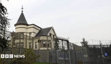 A white building with a turret behind a gated security fence