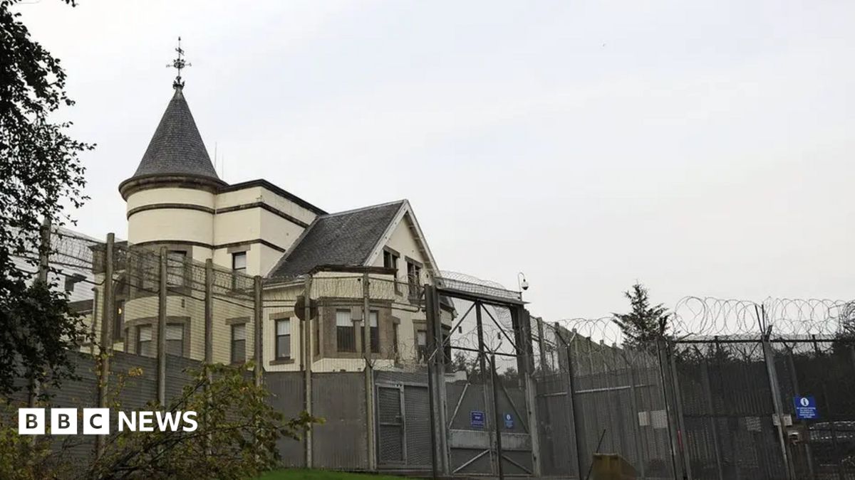 A white building with a turret behind a gated security fence