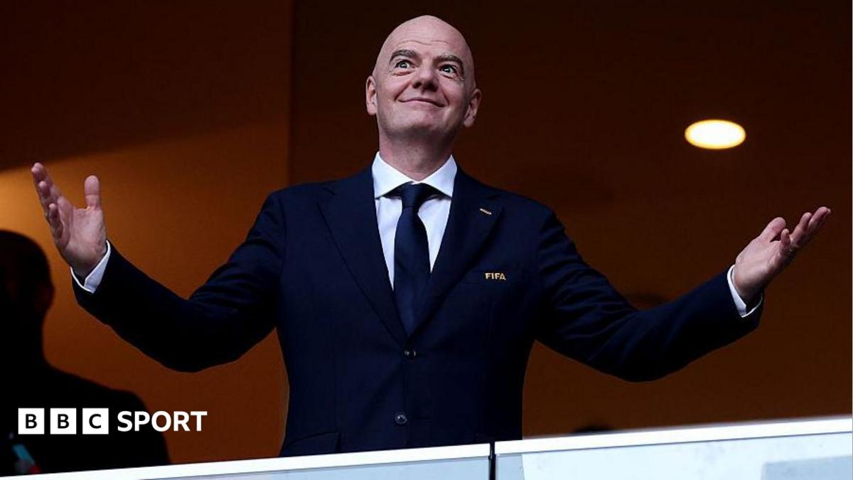 Gianni Infantino holds his arms out at each side with open palms, as he smiles while wearing a buttoned-up, dark smart jacket with FIFA written on its breast pocket