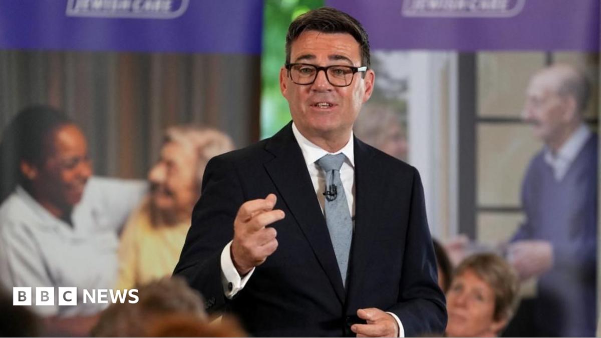 Andy Burnham is wearing a dark-coloured jacket, a white shirt, a tie and glasses. He is speaking to an audience who are not pictured.