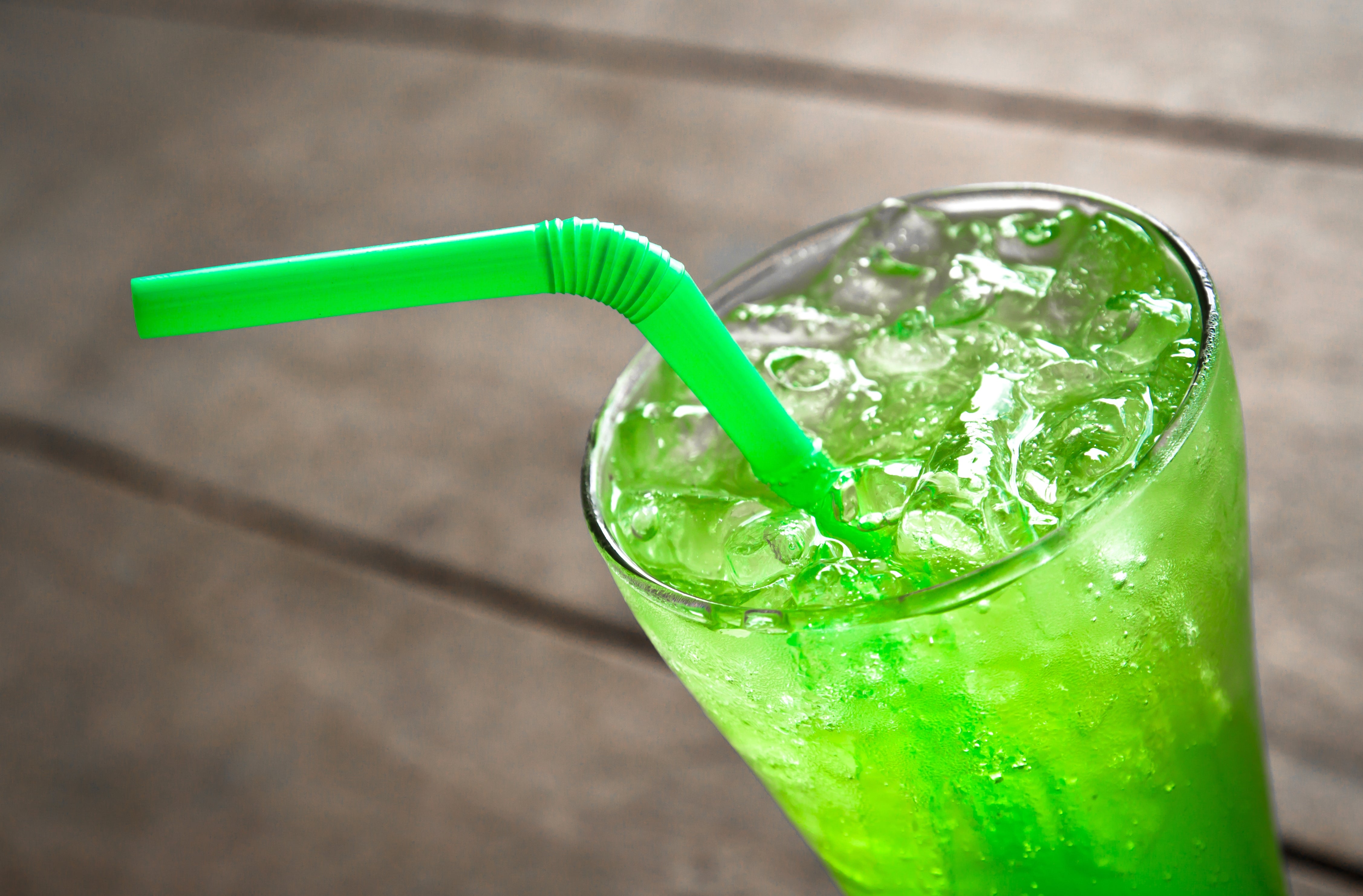 A glass filled with a green iced beverage and a green straw, placed on a wooden surface