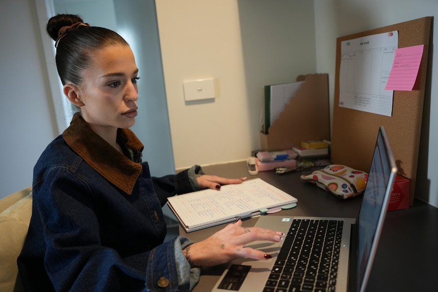 A young woman with dark hair sitting at a desk, using a laptop
