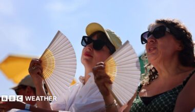Two women in sunglasses fan themselves, with blue sky and sunshine overhead