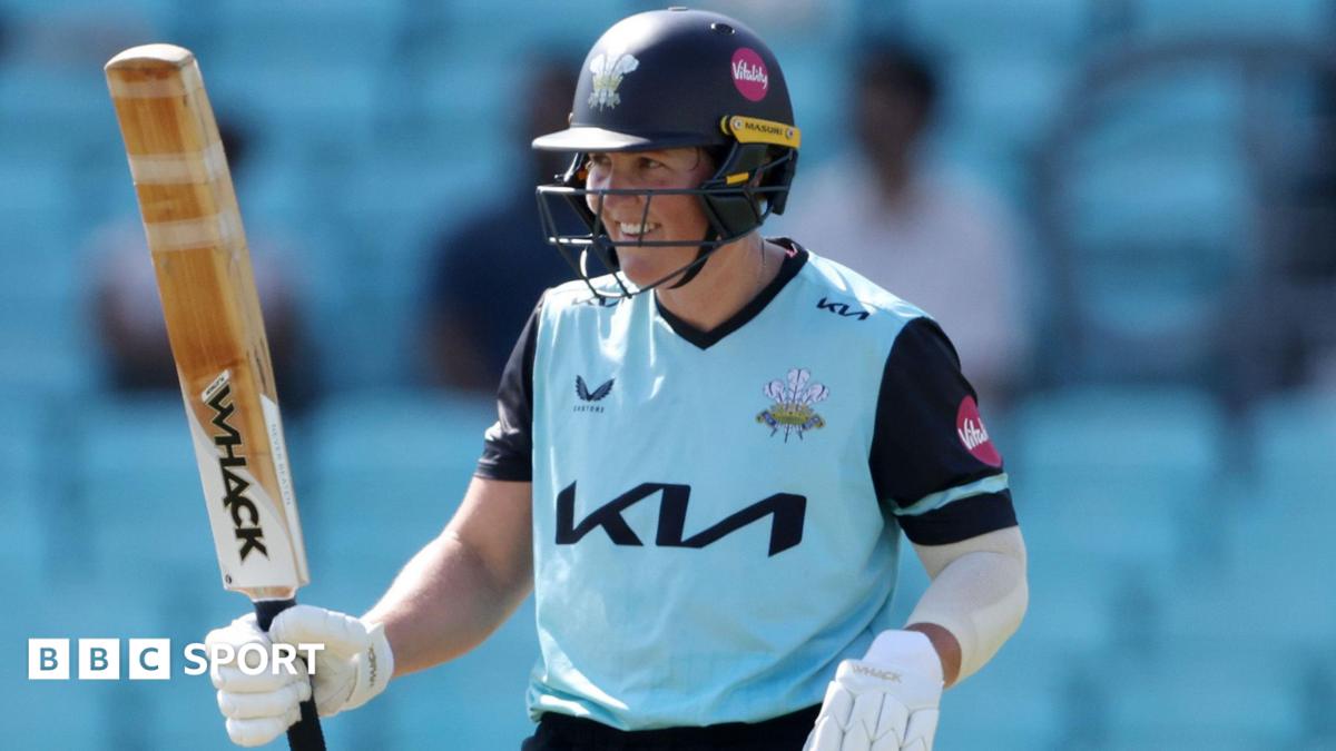 Laura Harris, wearing the Surrey Women's light blue shirt with navy sleeves and navy collar, raises her bat after scoring 50 in 15 balls against Warwickshire Bears