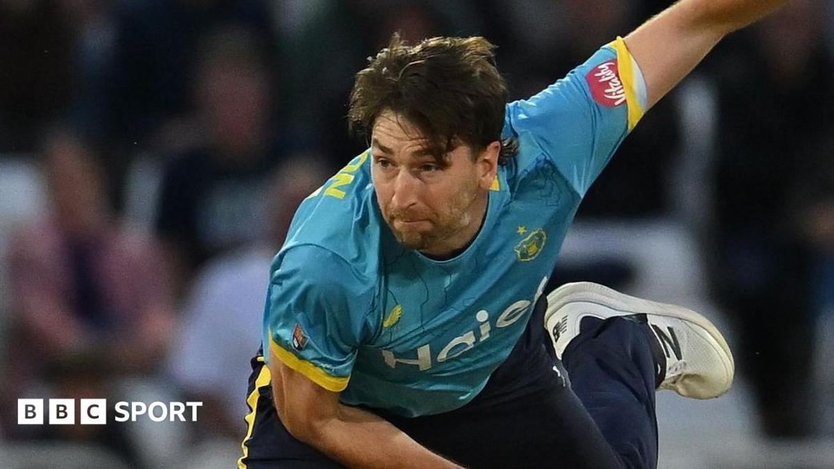 Bowler Richard Gleeson, wearing a blue shirt and navy trousers, watches after bowling a ball while playing cricket for Warwickshire Bears