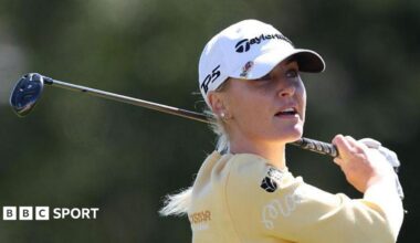Charley Hull, wearing a yellow top and white cap, with her golf club over her back left shoulder in her follow through