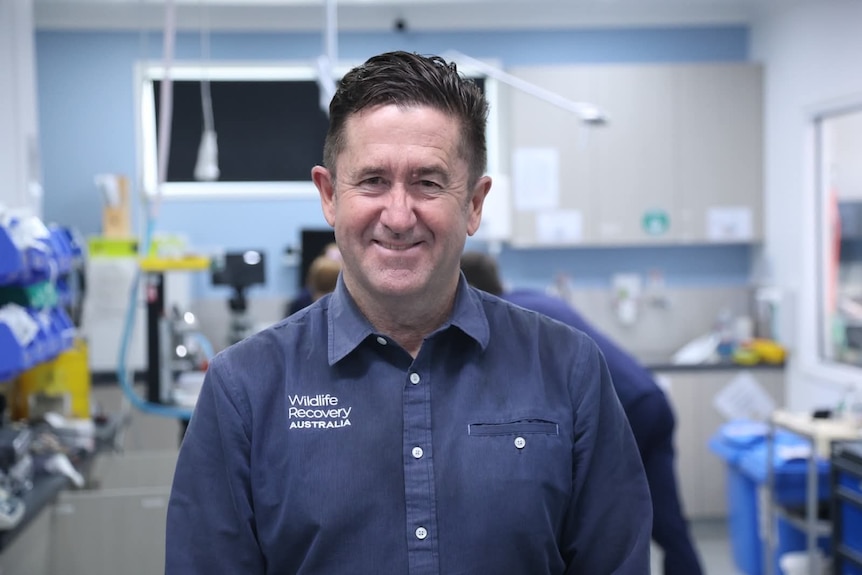 Stephen looks at camera, smiles, a hospital room behind.