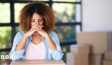 A woman with her head in her hands surrounded by boxes