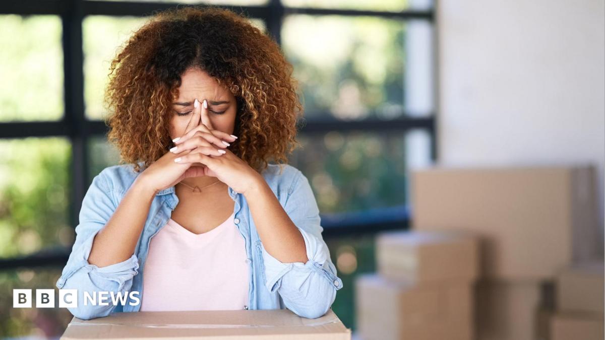 A woman with her head in her hands surrounded by boxes