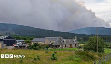 smoke over hills beyond farm buildings
