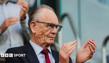 Ken Davy clapping his team, while wearing a navy suit with a crimson tie