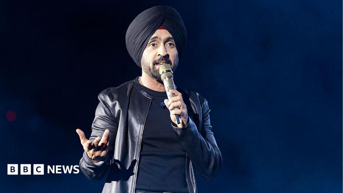 Diljit Dosanjh kicks off his Aura World Tour at BC Place on April 23, 2026, in Vancouver, British Columbia, Canada. He is wearing a black jacket over a black t-shirt and sporting a black turban, as he speaks on a microphone from the stage.