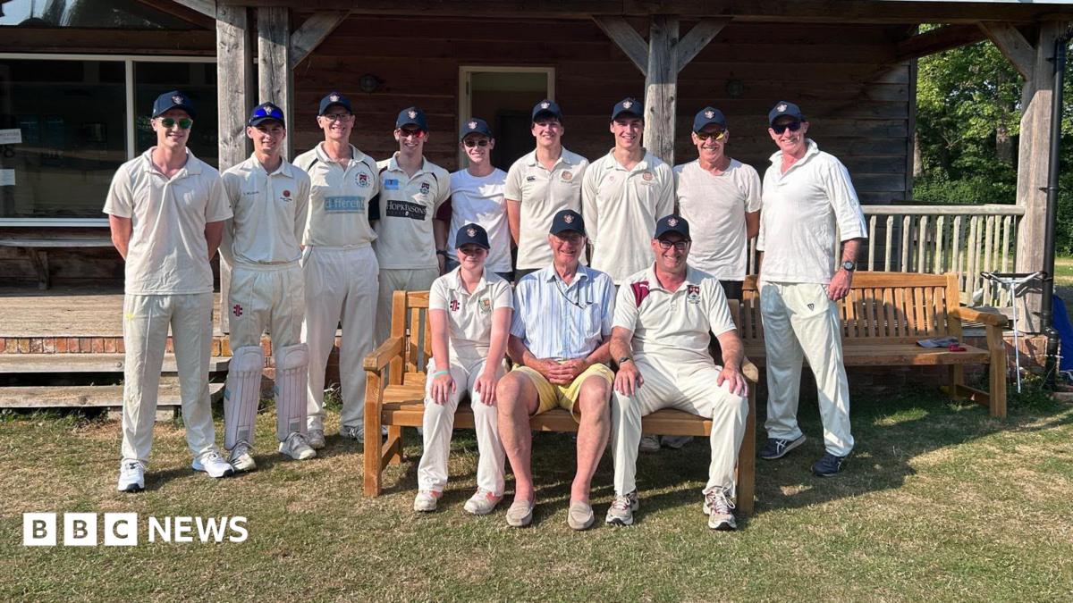 An older man surrounded by people in cricket gear.