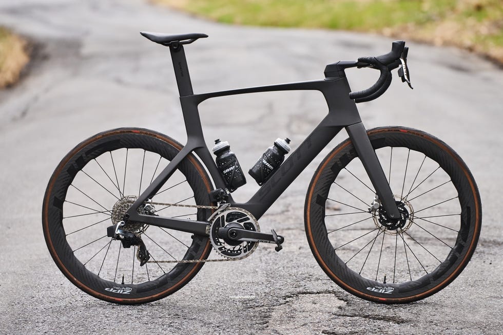 Sleek black road bike with water bottles, parked on a winding asphalt road surrounded by grassy areas.