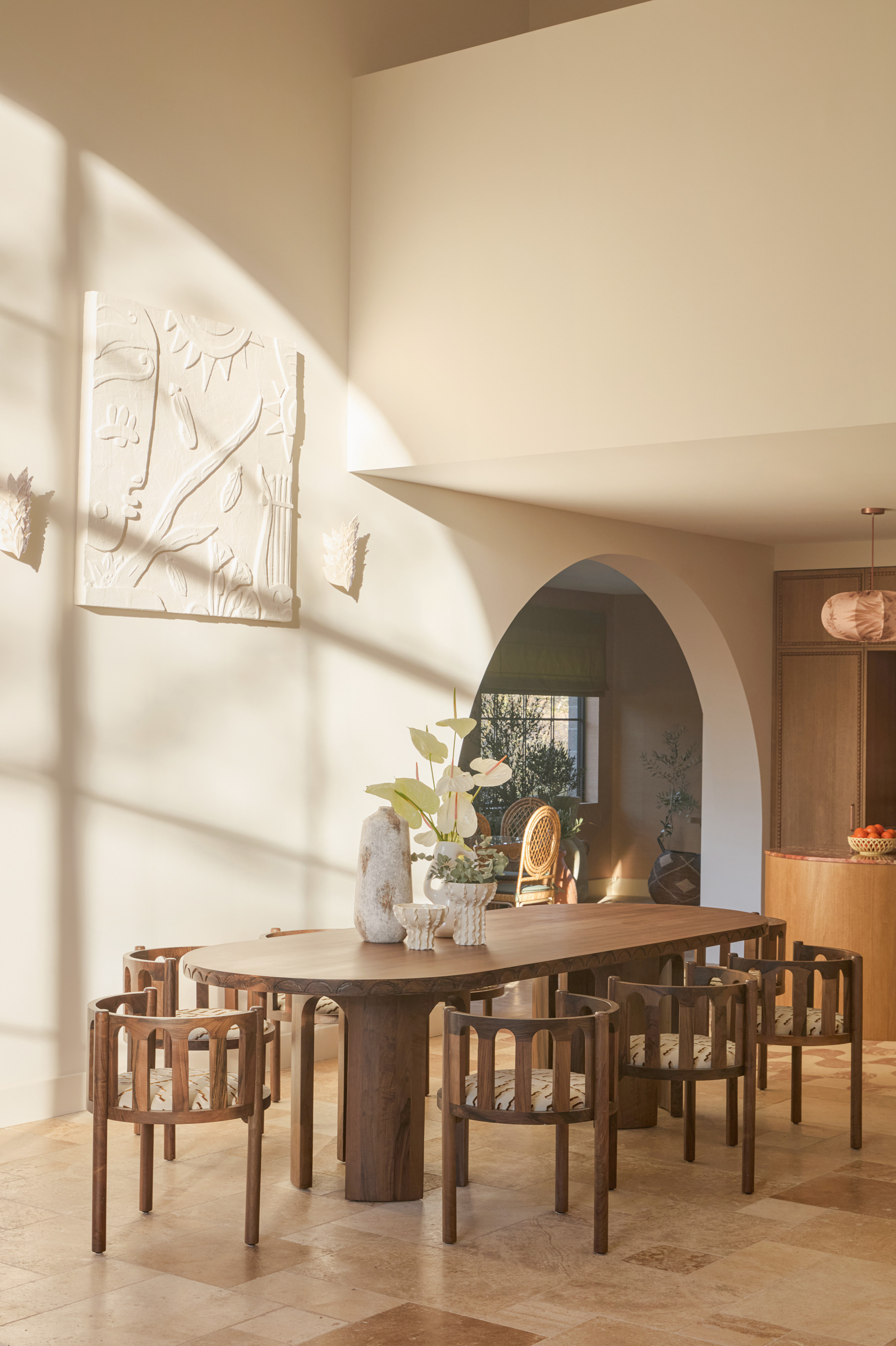 Dining room with plaster artwork on the wall, wood curved dining table and curved armchairs, brown and beige marble tiled floor