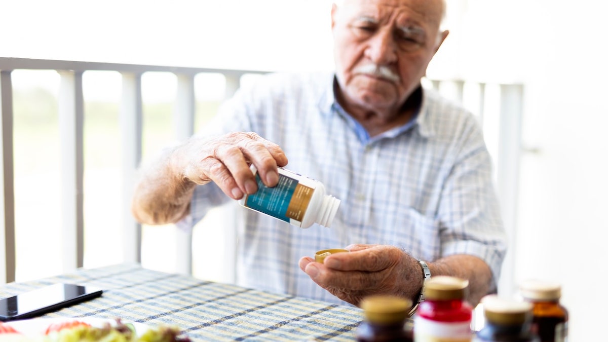 Elderly man taking a vitamin pill while seated
