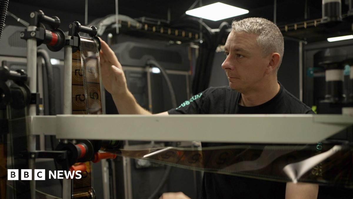 A man with silver hair adjusts a ruler over which film is looped
