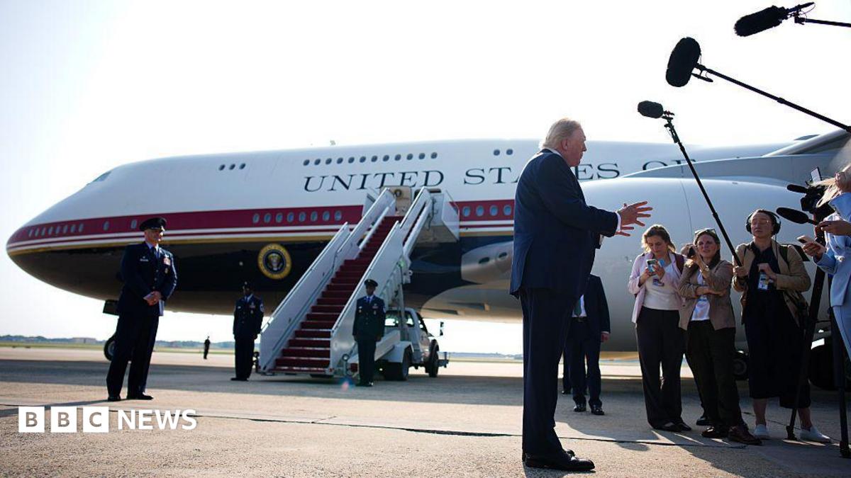 Trump stands in front of Qatari-gifted Air Force One and speaks to reporters who are holding boom microphones