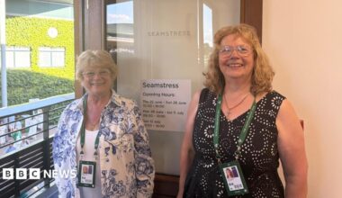 Erica Russell and Marlien Beets smile for the camera. They are stood beside an open door with the word 'seamstress' etched into its glass.