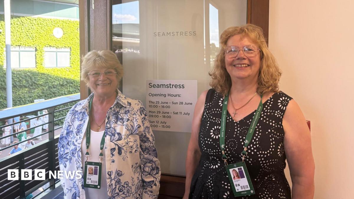 Erica Russell and Marlien Beets smile for the camera. They are stood beside an open door with the word 'seamstress' etched into its glass.