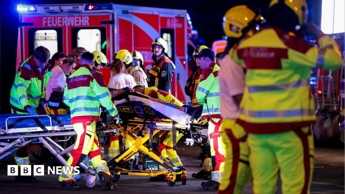A number of emergency services personnel standing near an ambulance, with a person on a stretcher