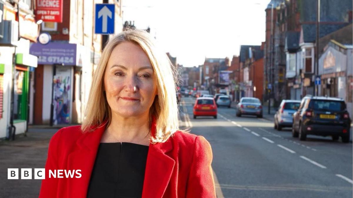 Portrait of MP Jo Platt standing on Railway Road, Leigh. She is wearing a red jacket and smiling.