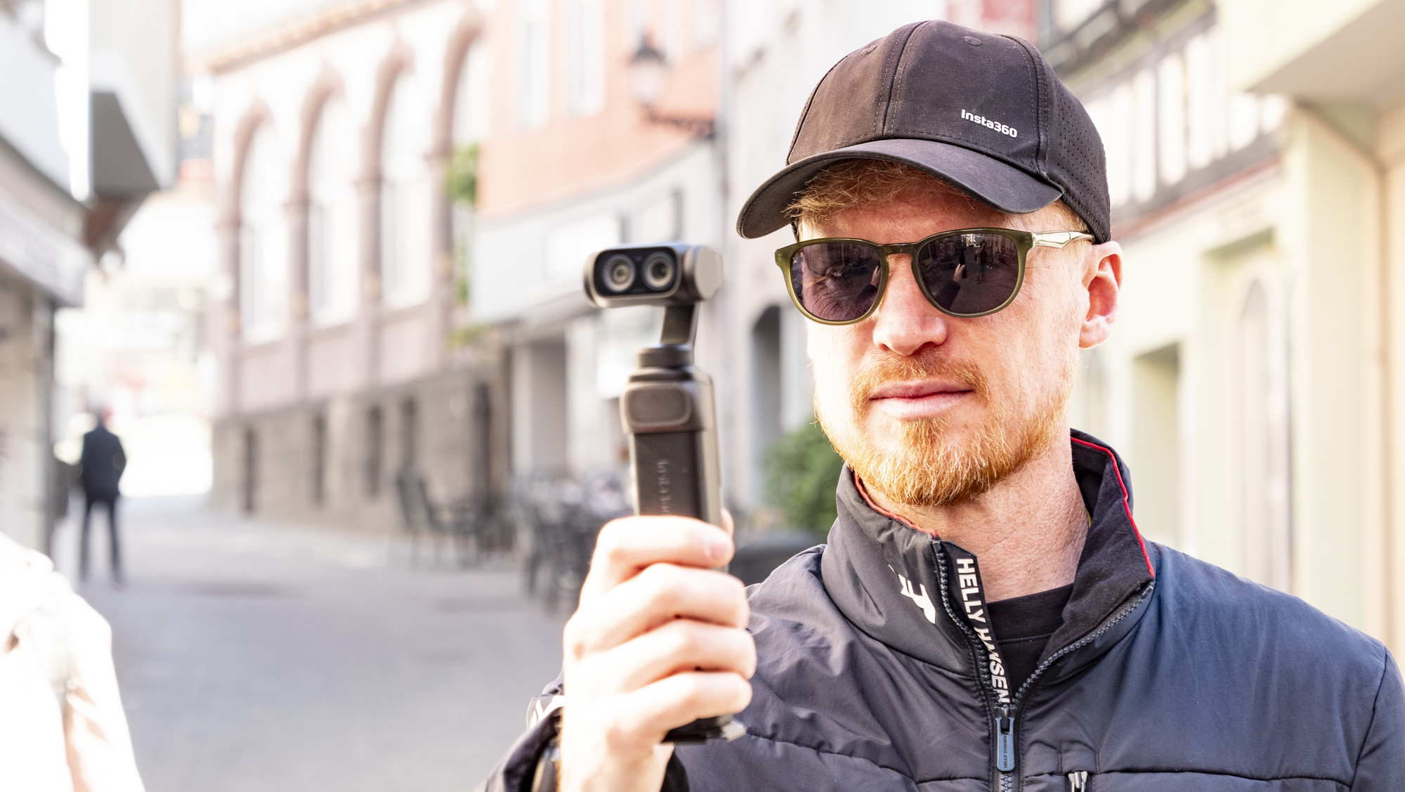 Man holding the Insta360 Luna Ultra vlogging camera on a sunny day in a old town