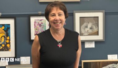 Dr Nicola Fox is stood, smiling, with a gallery of art behind her