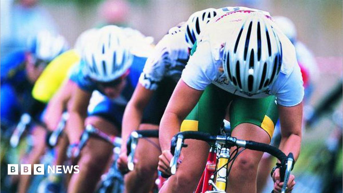 Three male cyclists with white tops and green shorts on a bike racing behind each other. All are wearing white cycling helmets.