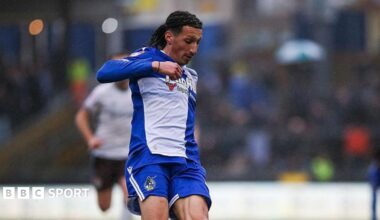 Yusuf Akhamrich in royal blue and white Bristol Roves kit looks down to control the ball