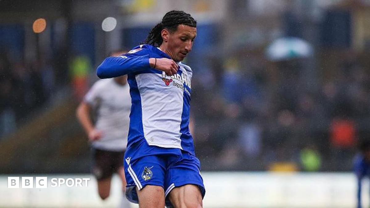 Yusuf Akhamrich in royal blue and white Bristol Roves kit looks down to control the ball