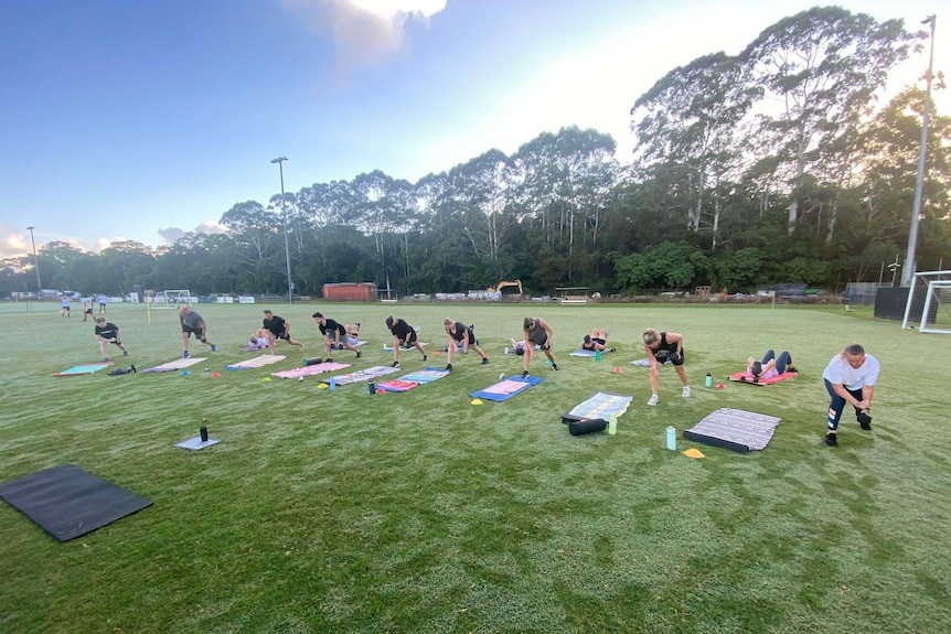 A group of people working on near exercise mats on a green grassy oval