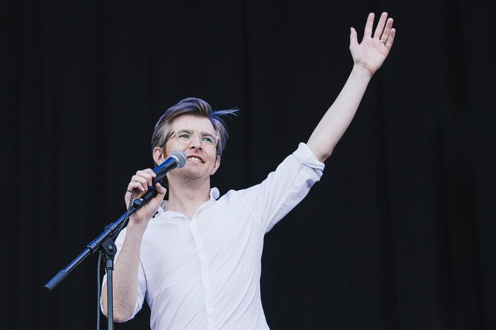 Latitude Festival 2015 - Day 4 Gareth Malone addresses a festival crowd with one arm raised, wearing glasses and a white shirt beside a microphone stand.