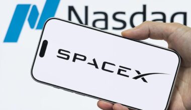 A phone with the SpaceX logo is being held up in front of a background with the Nasdaq logo.