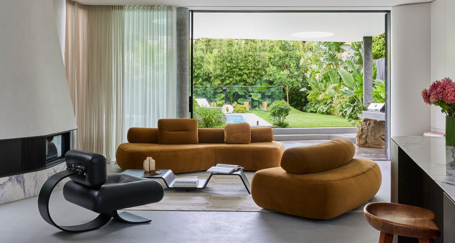 A bright living room with mustard sofas, a black leather chair, a multi-level coffee table, and a white rug