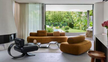 A bright living room with mustard sofas, a black leather chair, a multi-level coffee table, and a white rug