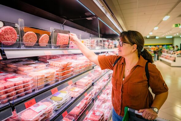 Woman buying groceries at supermarket, choosing a frozen meat package from the refrigerated section