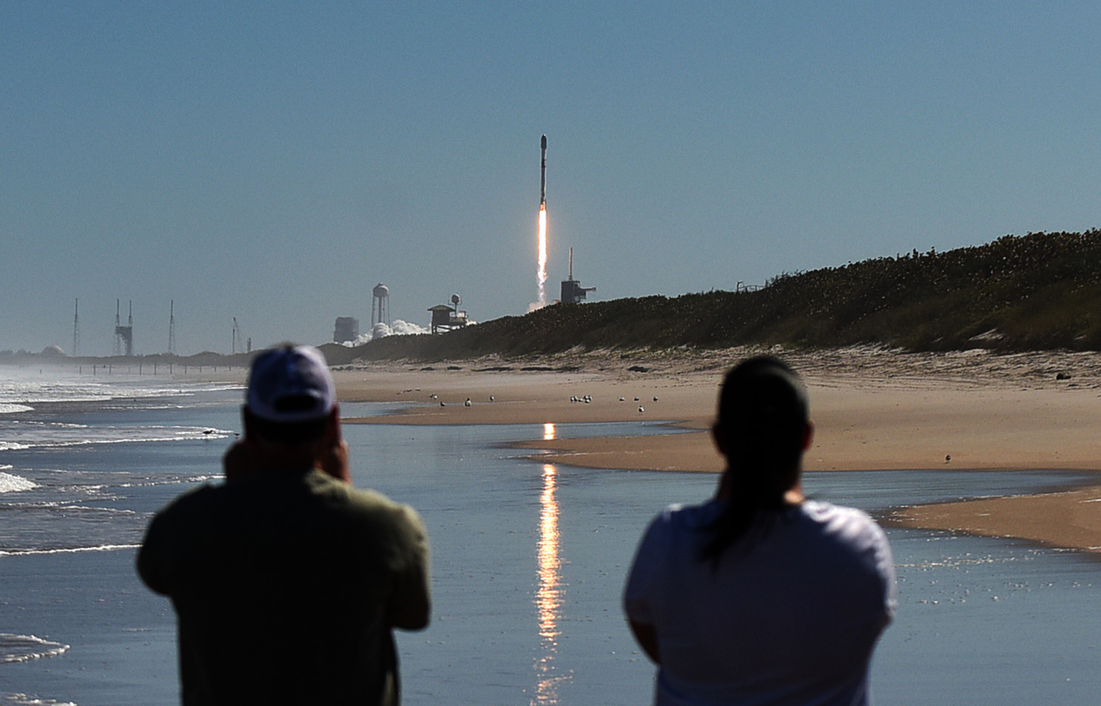 People watch from Canaveral National Seashore as a SpaceX Falcon 9 rocket launches from pad 39A at the Kennedy Space Center in Cape Canaveral, Florida.