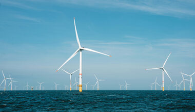 Multiple white wind turbines in the sea with clear blue skies
