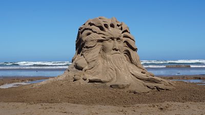 A sand sculpture of a man faces with long hair and a beard