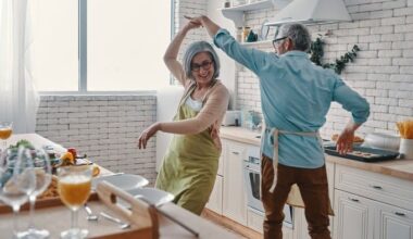 A mature aged couple dance together in their kitchen while they are preparing food in a joyful scene.