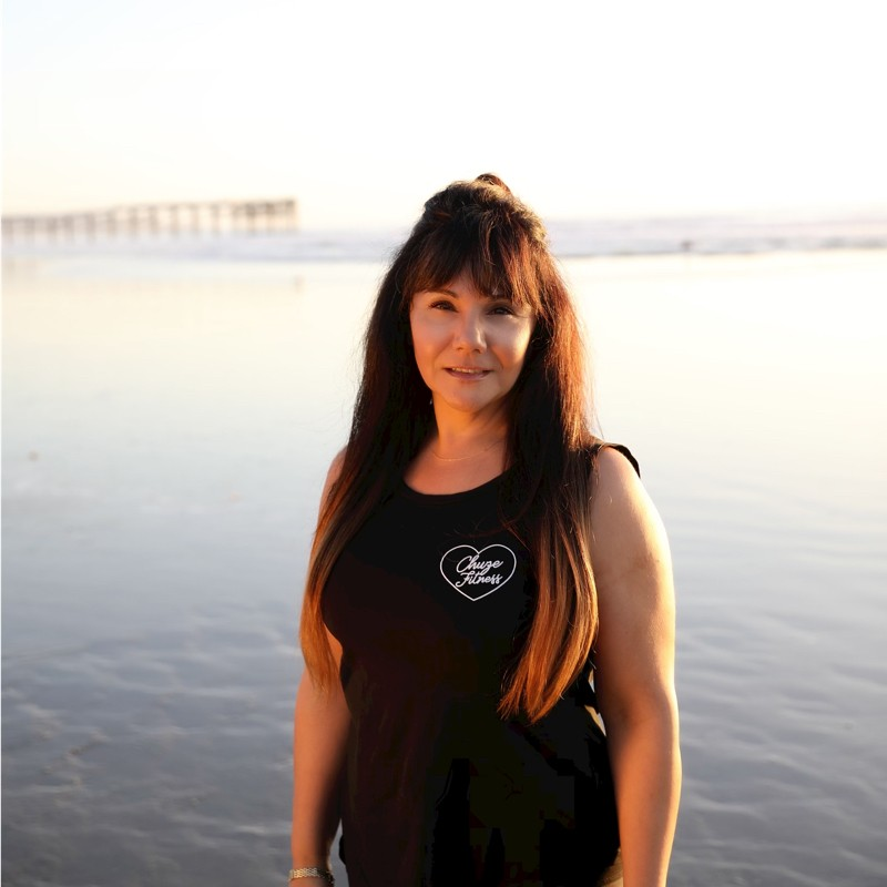woman facing the camera wearing a black vest and a body of water behind her