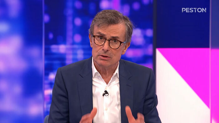Expert in a suit and white shirt, wearing glasses, speaks with a serious expression about a grim AI warning.