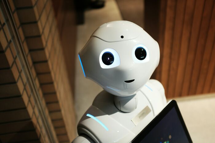 A white humanoid robot with glowing blue eyes and a tablet, representing the impact of AI.